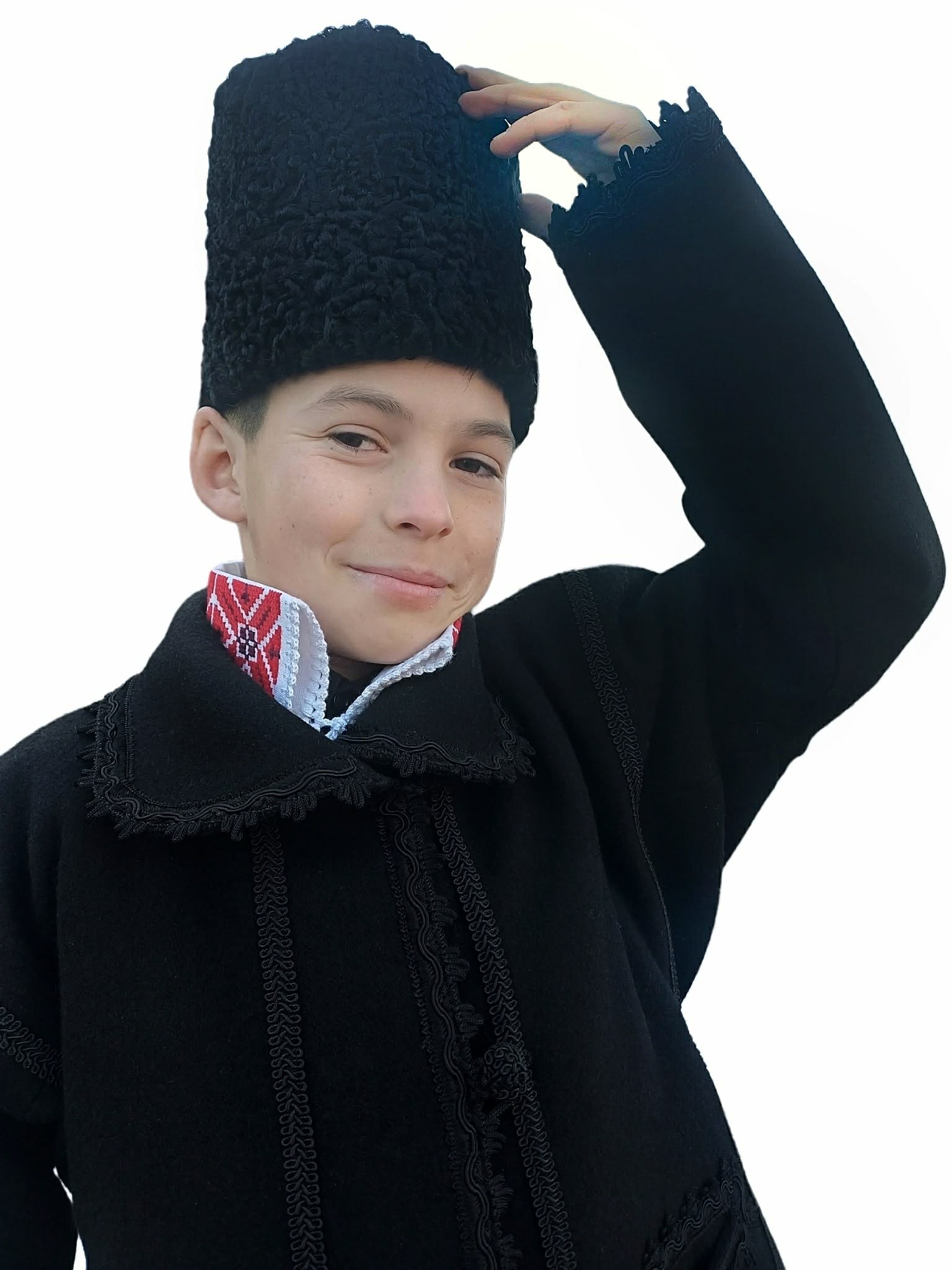 Băiat îmbrăcat în costum tradițional românesc, purtând cușmă (căciulă țărănească) din blană de miel, pe fundal alb