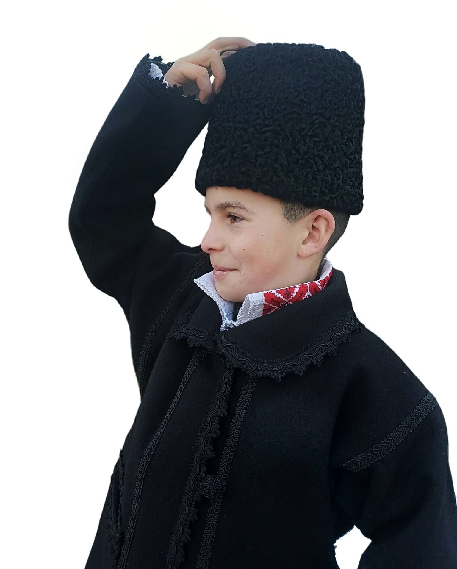 Băiat îmbrăcat în costum tradițional românesc, purtând cușmă (căciulă țărănească) din blană de miel, pe fundal alb